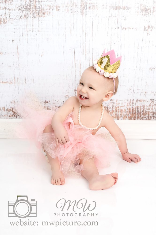 A baby girl wearing a pink tutu and crown.