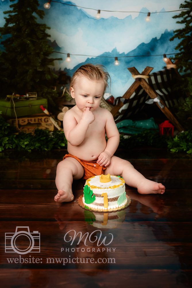 A baby sitting on the ground with a cake in front of him.