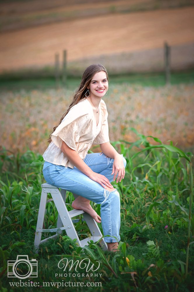 A woman sitting on top of a stool in the grass.