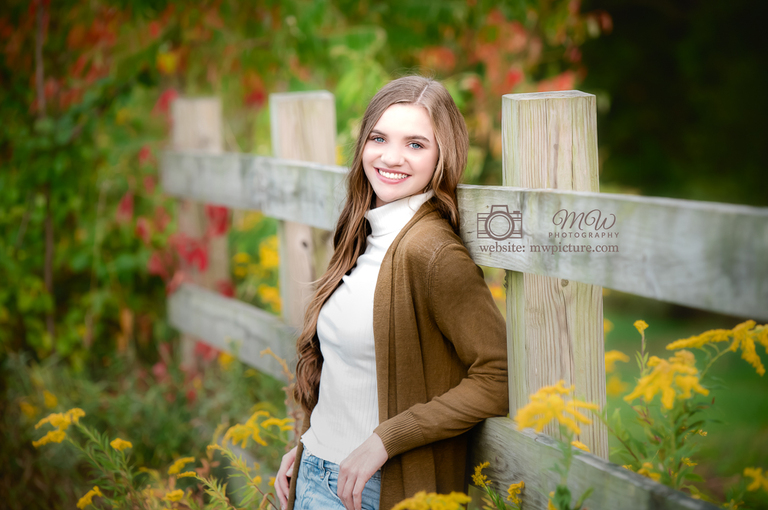 A girl standing in front of a fence with flowers.