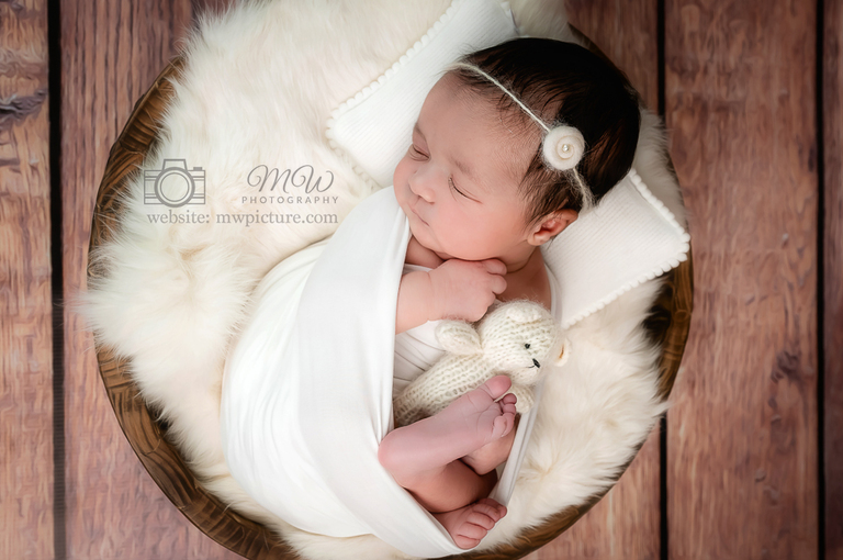 A baby is wrapped in white blanket and holding a teddy bear.