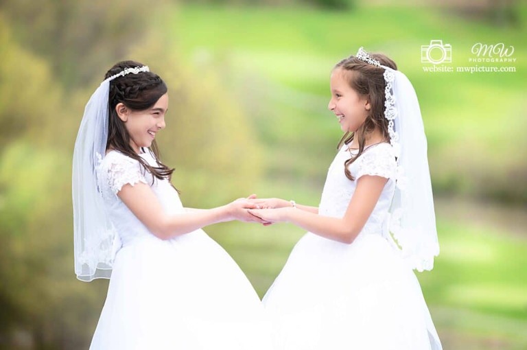 Two young girls in white dresses holding hands.